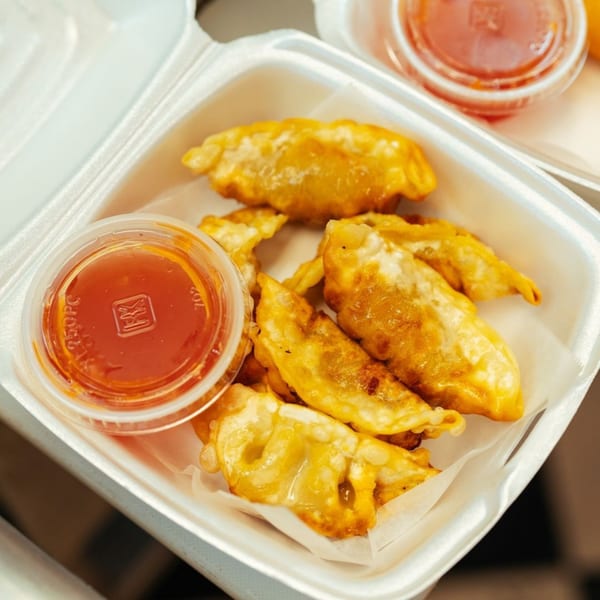 Golden-fried gyoza dumplings with sweet chili dipping sauce in a white takeout container from Tokyo Express Grill.