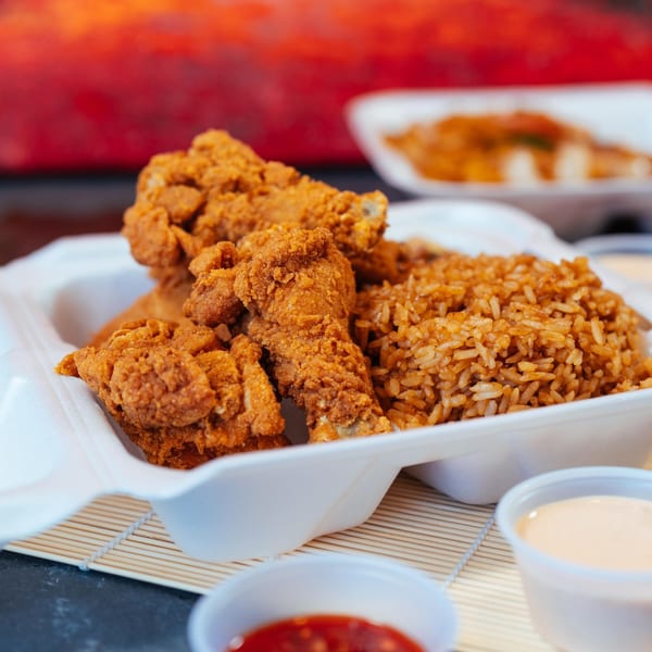 Crispy fried chicken and seasoned rice in a white takeout container with dipping sauces.