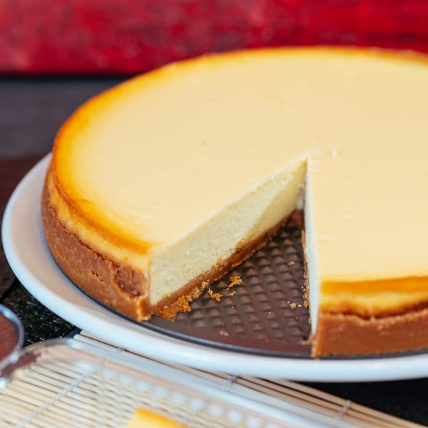 A whole cheesecake with a slice removed, showing its creamy texture and crust.